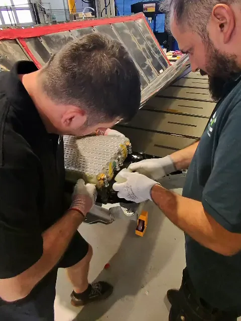 Two technicians opening a battery module, exposing the cylindrical cells.