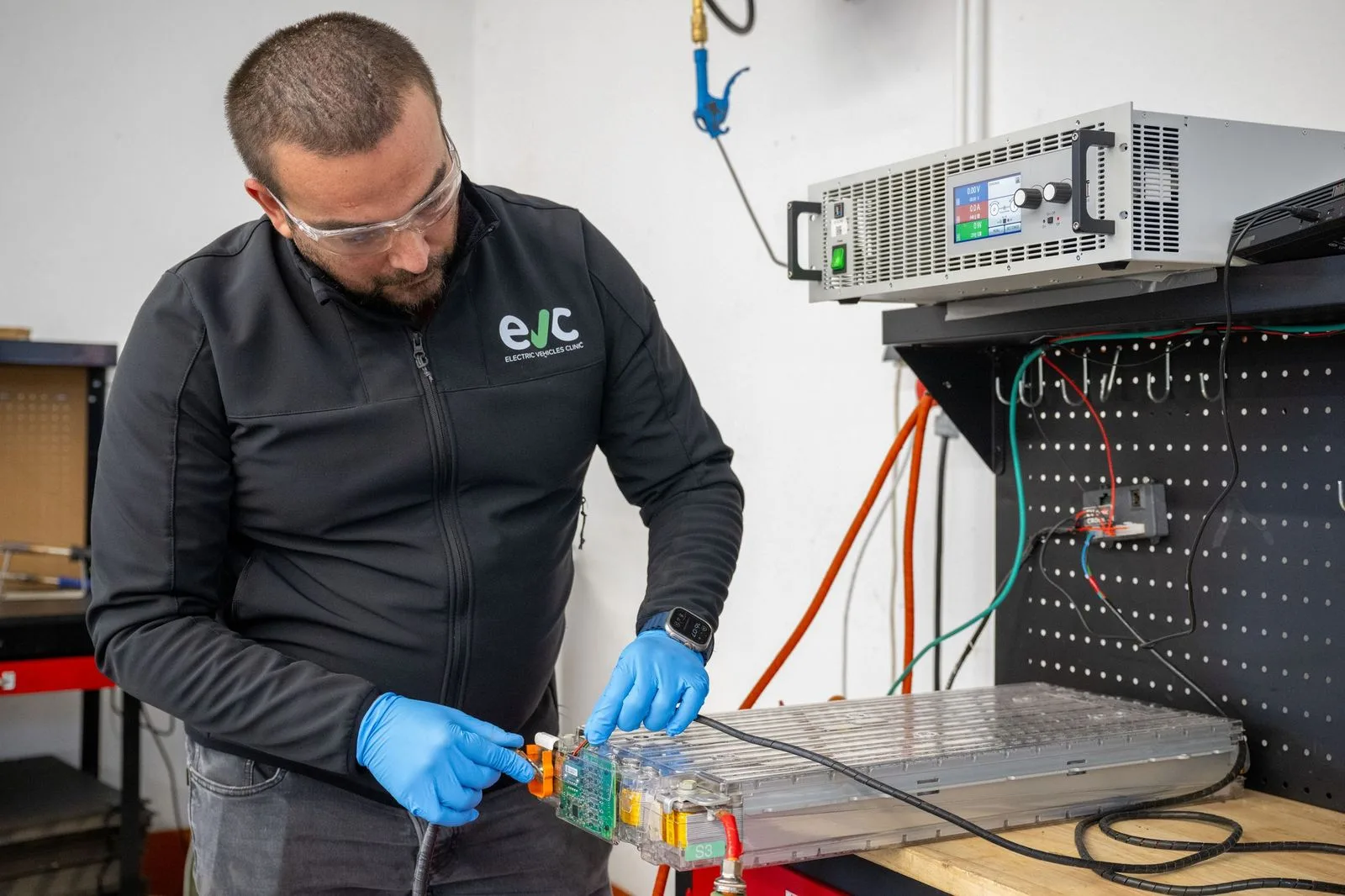 Technician measuring a battery module on the bench beside a laboratory power supply.